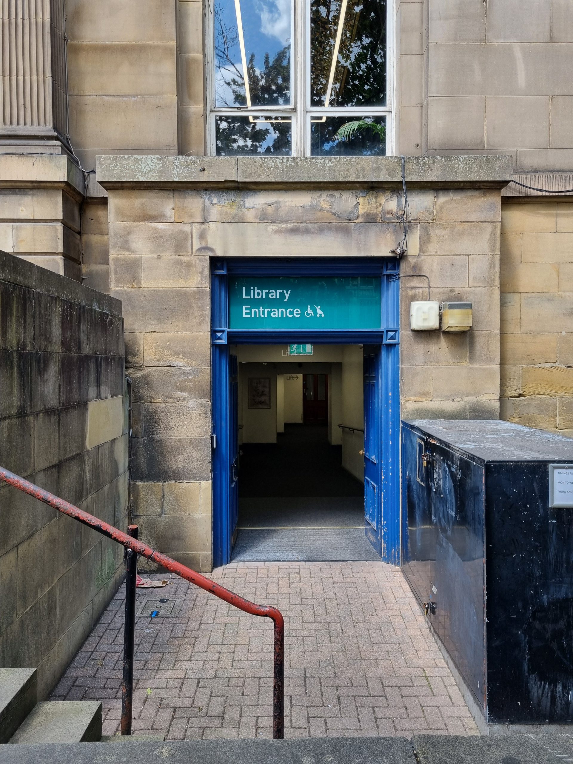 Accessible entrance to library at lower ground floor level. Doors are blue and open, with "Library Entrance" written above, with a wheelchair and pushchair graphic.